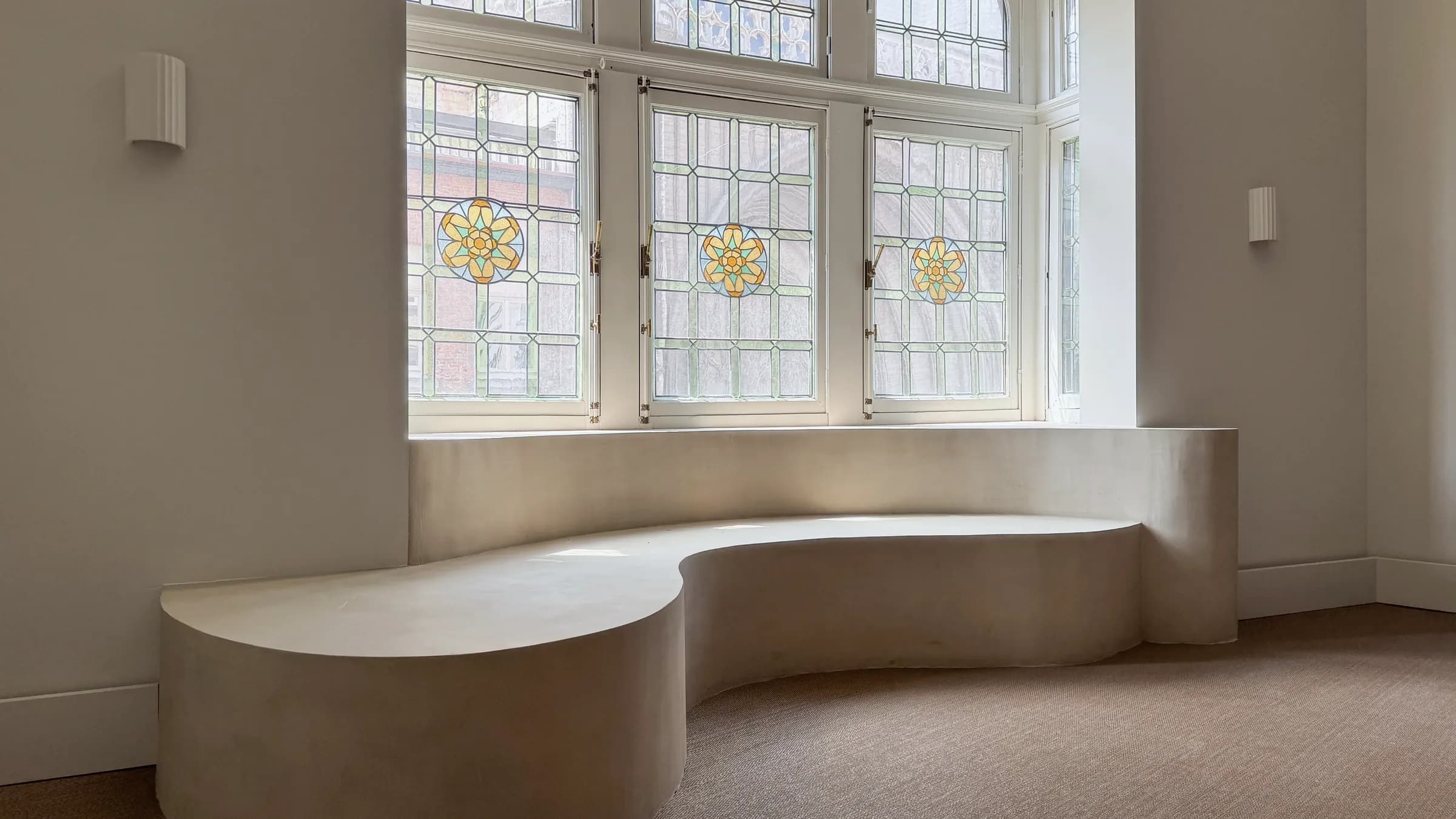 De salon op de eerste verdieping van Huis Pollet: een gebogen zitbank onder hoge glas-in-loodramen